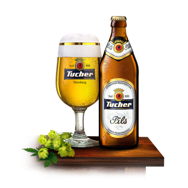 A beer glass and a bottle sit on a wooden table, surrounded by hop branches.