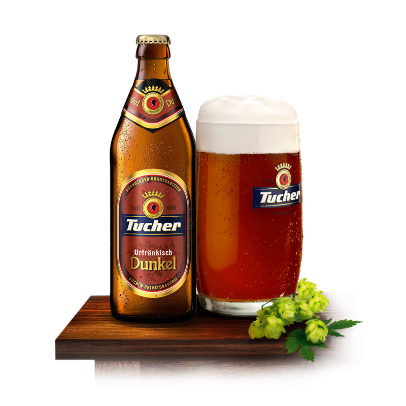 A dark beer bottle stands next to a full glass of beer on a wooden table.