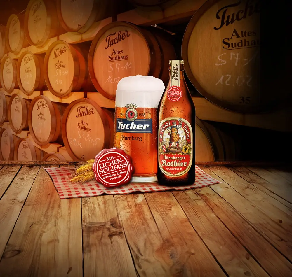 A glass of beer and a bottle stand in front of barrels on a wooden table.