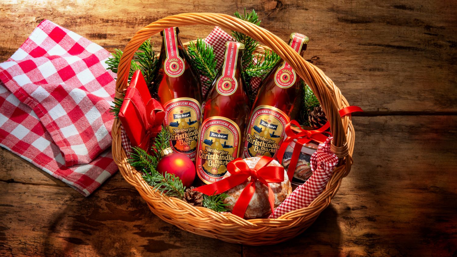 A Christmas hamper full of beer bottles and a stollen, decorated with red ribbons and fir branches.