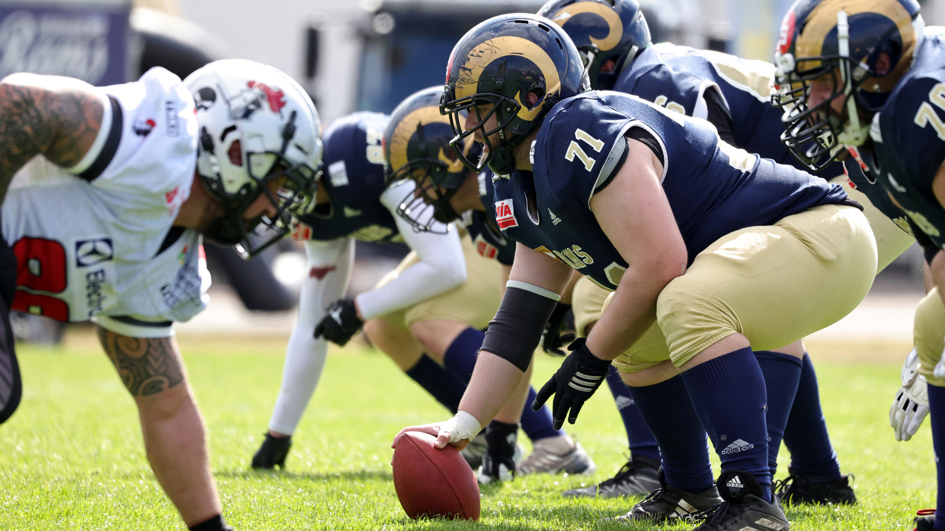 Two football teams face each other in attacking positions, and a player prepares for the snap.