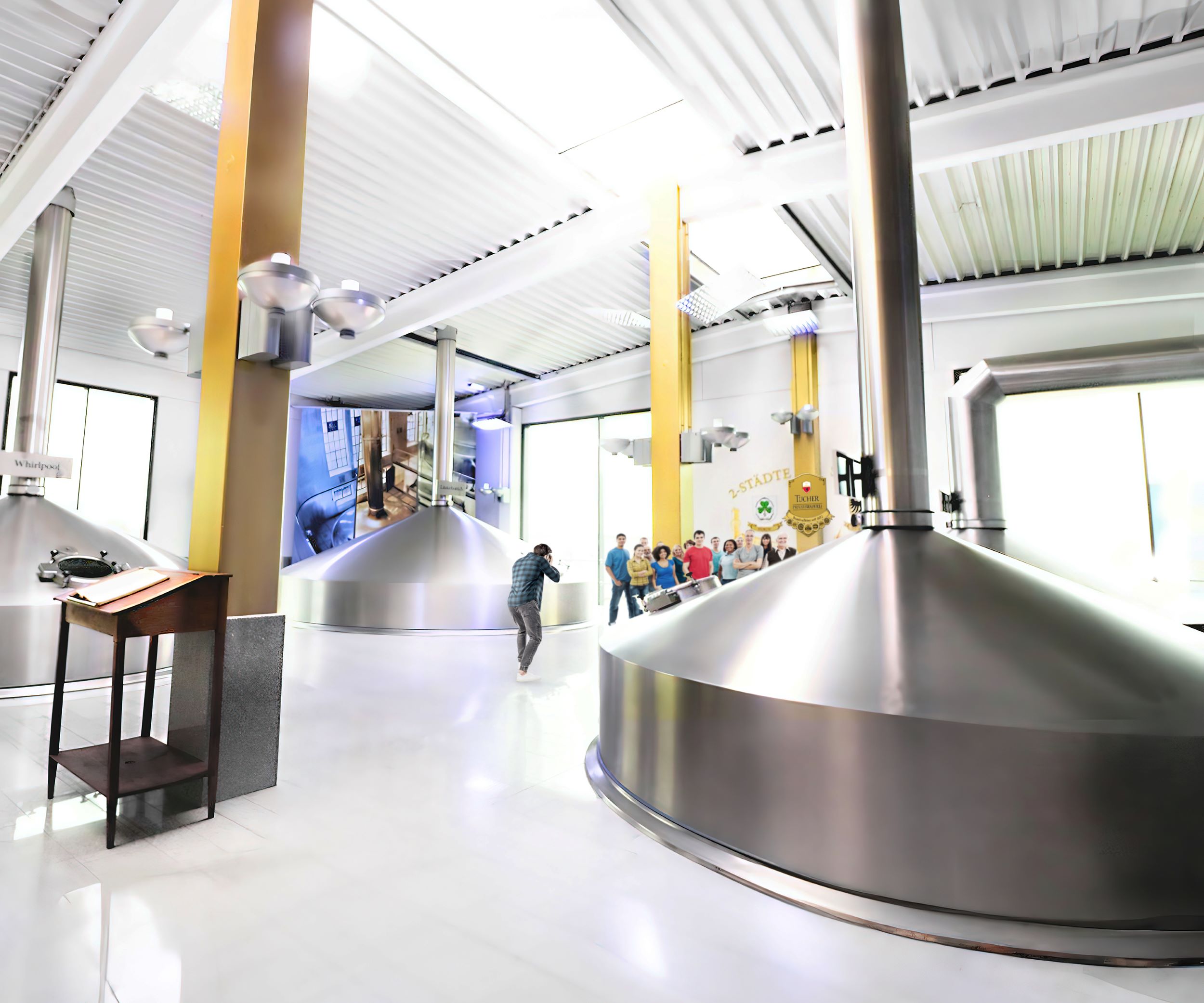A person photographs large brew kettles in an industrial brewery room.