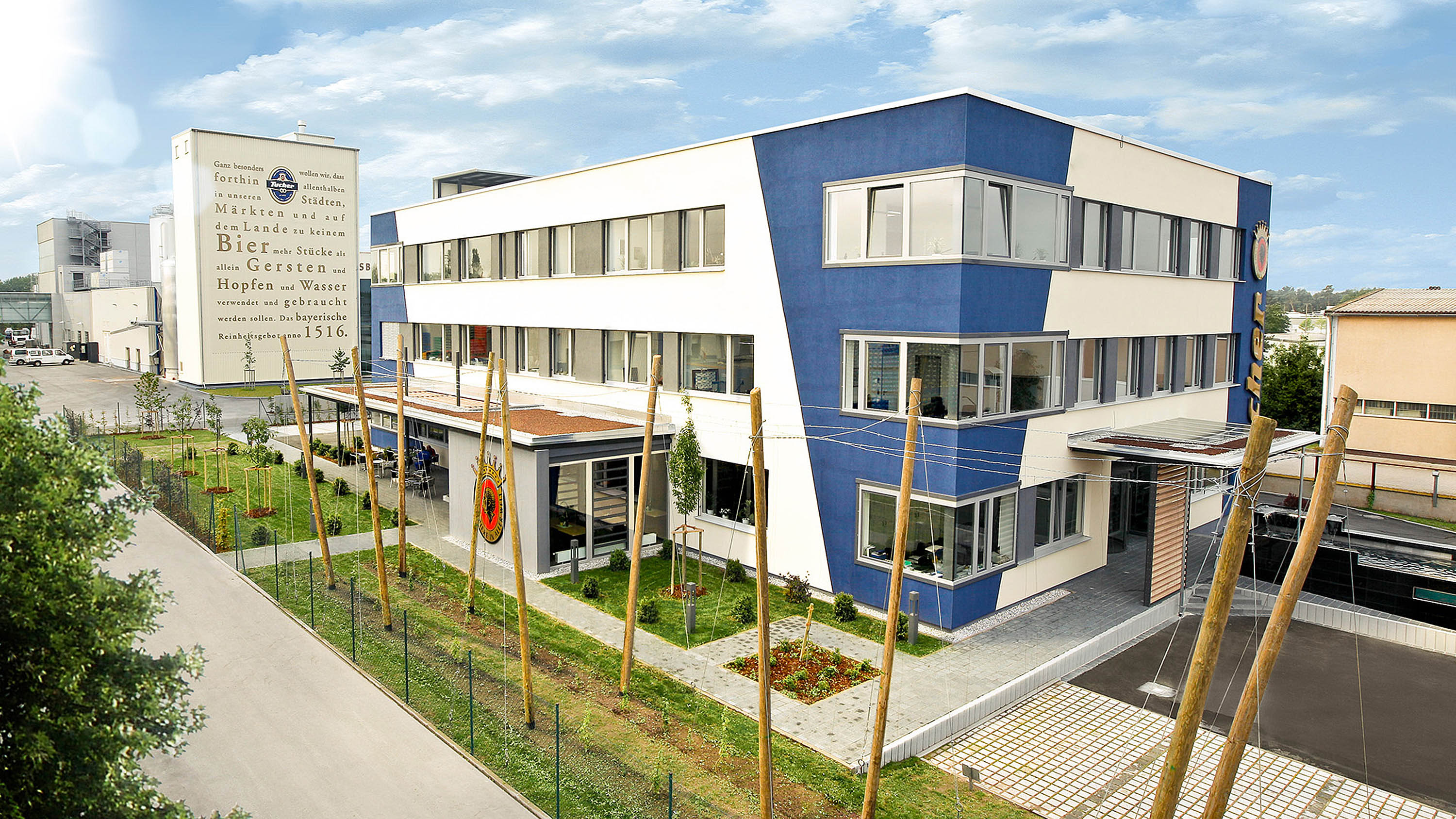 Modern brewery with several buildings and a landscaped garden is depicted. The main tower presents information texts.